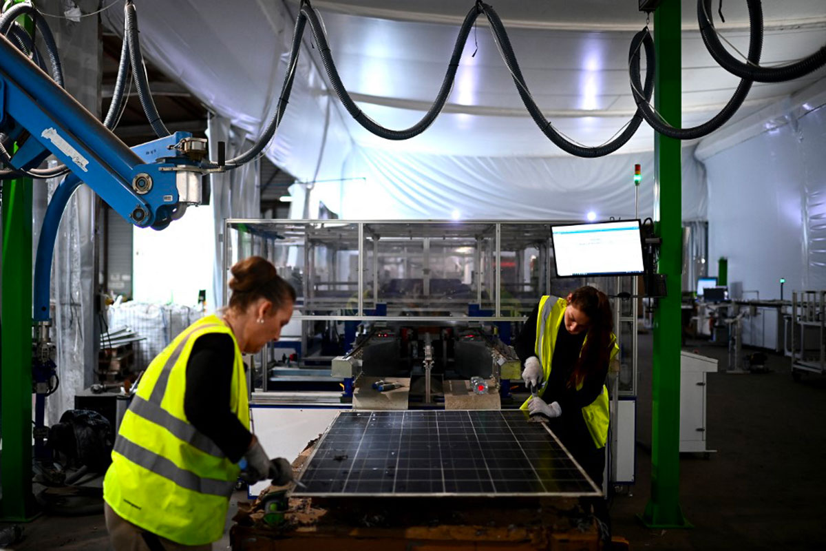 Des employés préparent un panneau solaire usé pour le charger dans une machine qui permet son démontage pour le recyclage des pièces de l'entreprise Envie 2E à Saint-Loubes, dans le sud-ouest de la France. Crédit Christophe ARCHAMBAULT / AFP